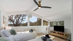 A modern bedroom with two beds, a ceiling fan, a TV, and large windows offering a mountain view. - Redscape, Near Great Hiking, Views, Hot Tub, Firepit-Charming Design (Sedona)