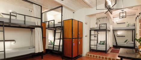 A dormitory room with bunk beds, a wooden cabinet, a desk, and a ceiling fan.