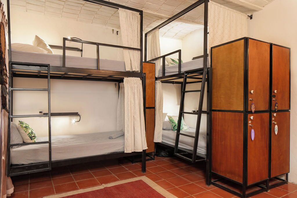 A dormitory room with bunk beds, a wardrobe, and a red rug.