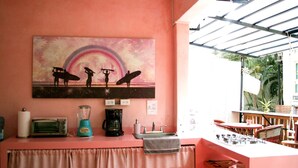 Un coin cuisine avec un mur rose, un tableau représentant des surfeurs et une vue sur l’extérieur.