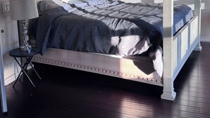 A bedroom with a four-poster bed, a bedside table with a lamp, and a dark wooden floor. - Spacious 4/bedroom house in delightfulneighborhood (Corona)