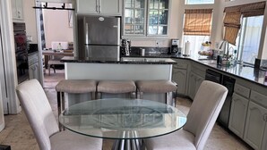 A modern kitchen with a central island, stainless steel appliances, and a glass dining table with four chairs. - Spacious 4/bedroom house in delightfulneighborhood (Corona)