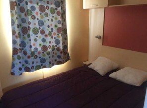 A bedroom with a bed, pillows, a nightstand, a wall-mounted cabinet, and a curtain with a polka dot pattern. - ZEcamping 3* piscine chauffée hammam sauna locatif TV 26m2 2 pers (Verruyes)