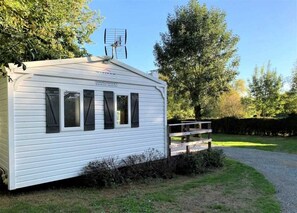 A white mobile home with a satellite dish, a gravel driveway, and a wooden deck. - ZEcamping 3* piscine chauffée hammam sauna locatif TV 26m2 2 pers (Verruyes)