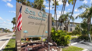 Schild für Sea Club Condominiums in der 1925 Gulf Blvd, mit amerikanischen Flaggen und Palmen.