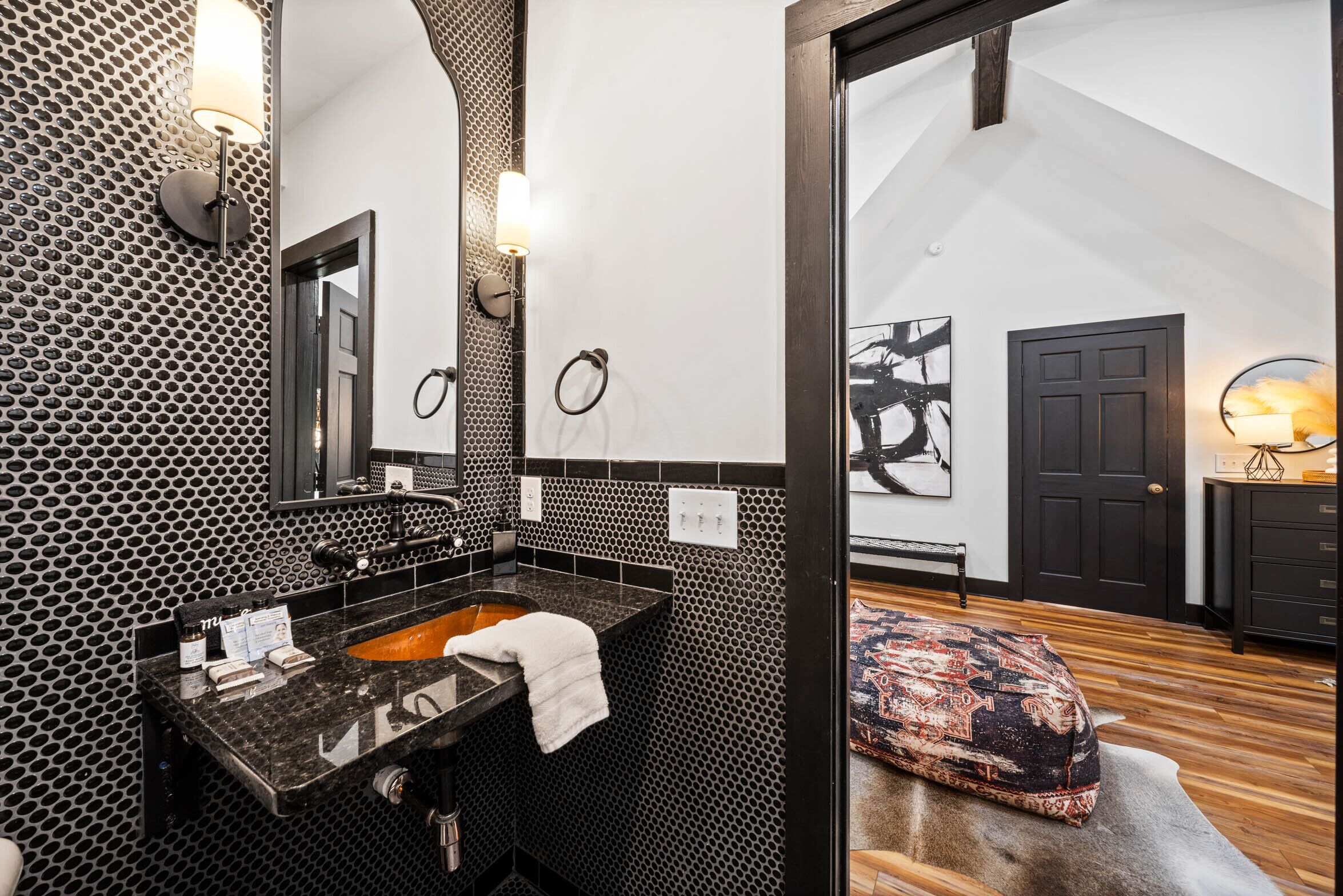 Une salle de bain moderne avec un mur orné d’un motif noir et blanc, un grand miroir et un lavabo avec une serviette.