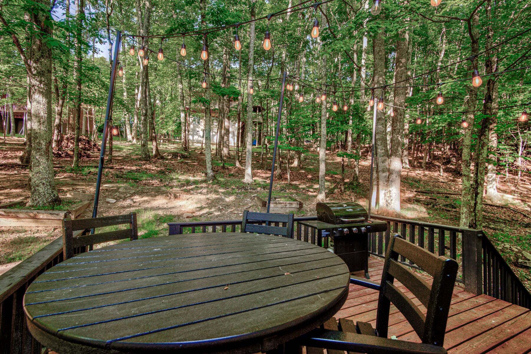 A deck with a round table and chairs, surrounded by a forest.