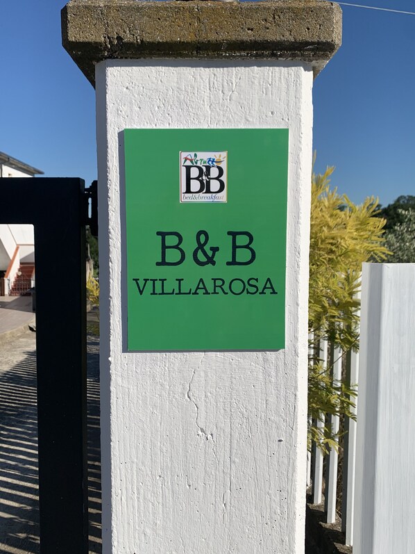 A sign on a white pillar with a green label that reads "B&B VILLAROSA" and a logo above it. - B&B VILLAROSA - your dream vacation between sea and mountains (Abruzzo)