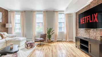 Un salon moderne avec un mur en briques, un grand écran de télévision affichant le logo « NETFLIX », un canapé, une table basse et un plancher en bois.