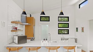 A modern kitchen with a central island, wooden chairs, pendant lights, and framed pictures on the wall. - East Austin + Private Pool - Eastside Palm Combo! (Austin)