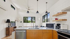 A modern kitchen with a central island, wooden cabinets, a built-in microwave, and a coffee maker. - East Austin + Private Pool - Eastside Palm Combo! (Austin)