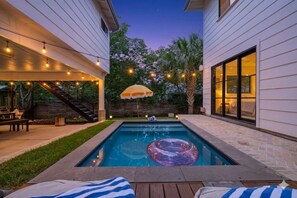 A swimming pool with a floating ring, surrounded by a deck with string lights and a covered seating area.