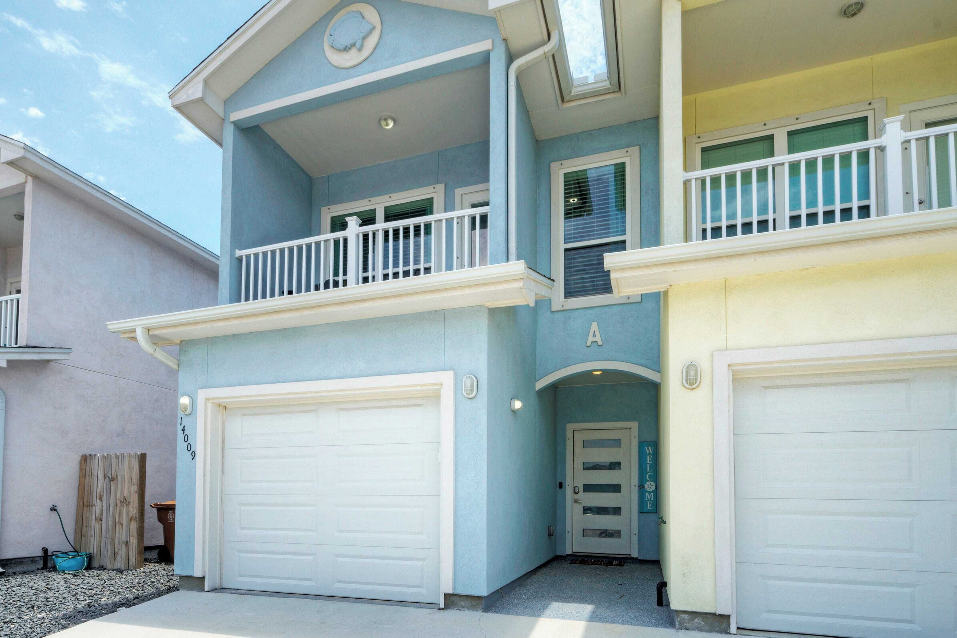 Une maison à deux étages avec un balcon, deux portes de garage et une pancarte de bienvenue.