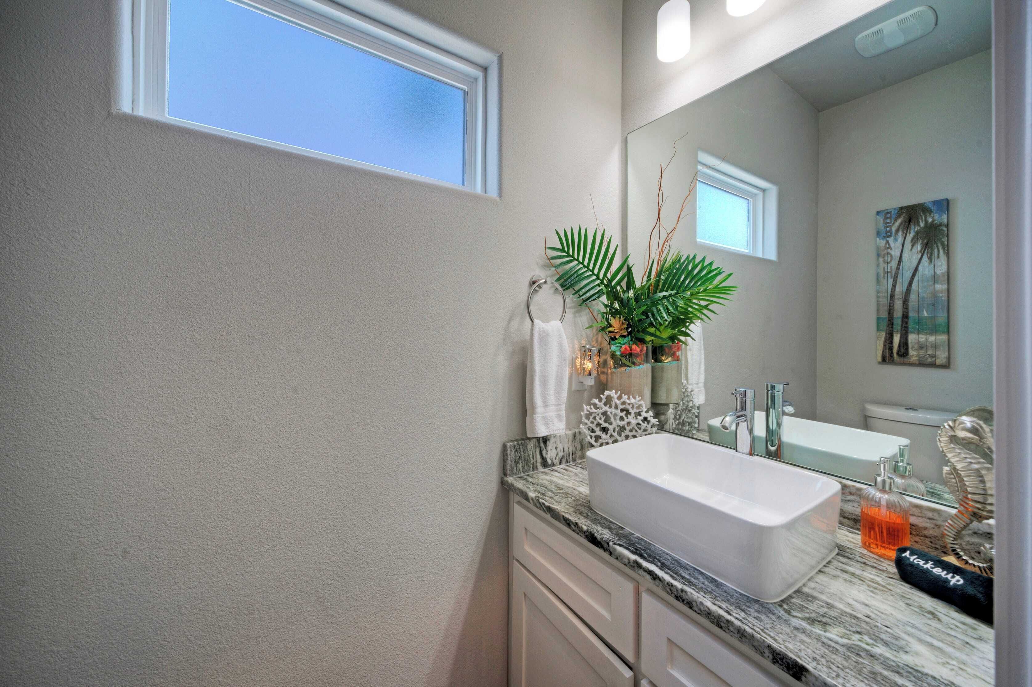 A bathroom with a white sink, a large mirror, and a window above the sink.