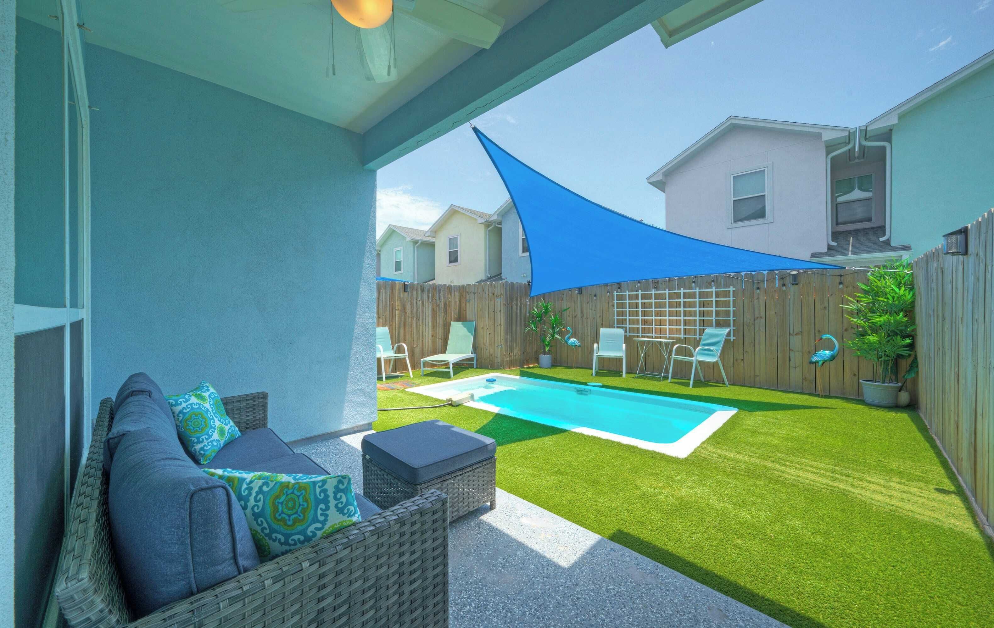 A backyard with a swimming pool, artificial grass, a wooden fence, and outdoor furniture.