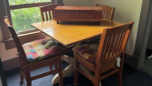 Un coin repas avec une table et des chaises en bois, une fenêtre donnant sur un paysage verdoyant et un sol recouvert d’une moquette.