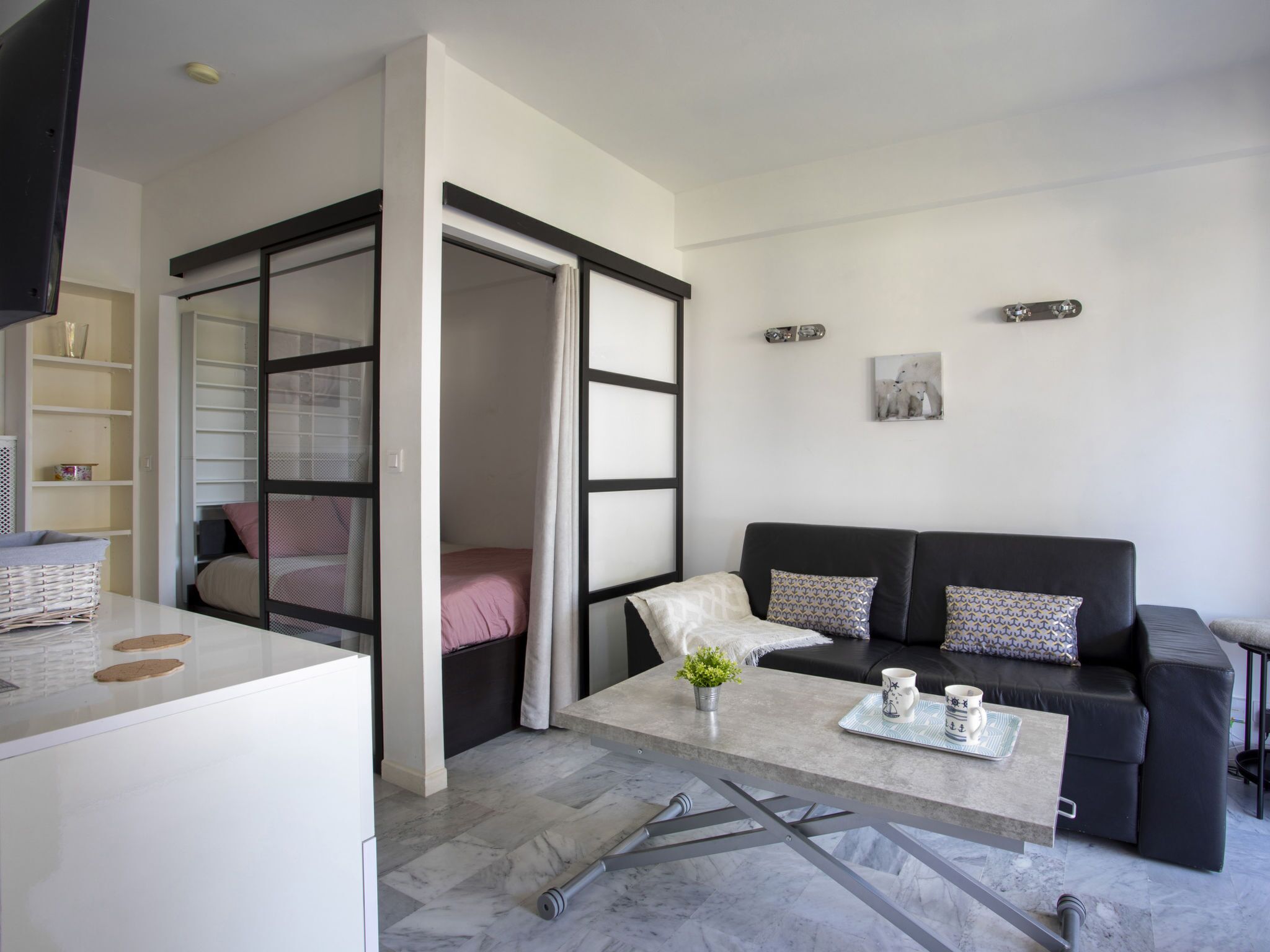 A modern living room with a sofa, a coffee table, and a sliding door leading to a bedroom.