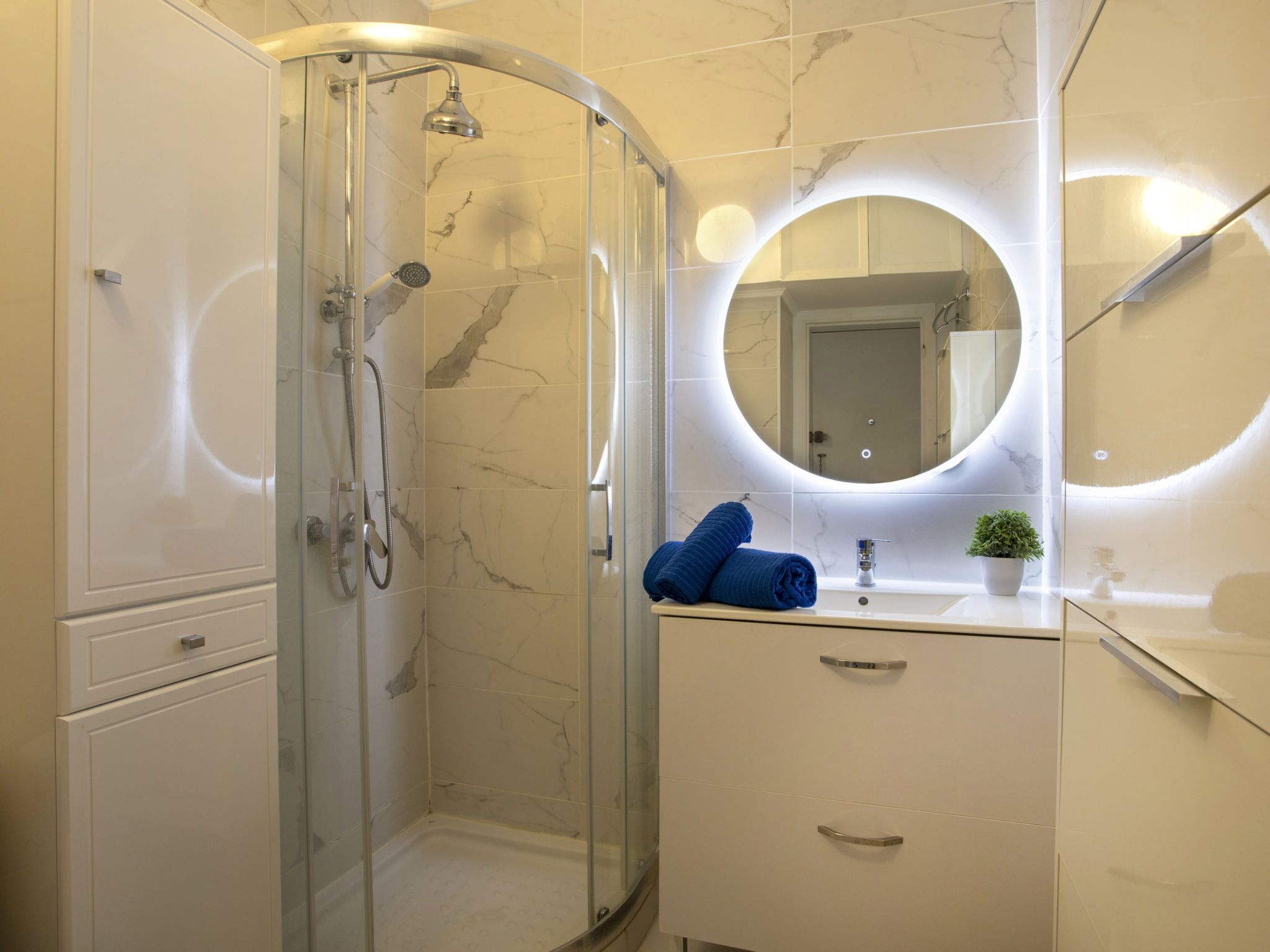 Un bagno moderno con doccia vetrata, un mobile lavabo con specchio e una piccola pianta in vaso.
