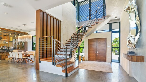 A spacious interior with a modern staircase, a dining area, and a large window providing a view of the outdoors.
