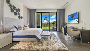 A modern bedroom with a large bed, a desk, and a view of a garden.