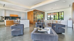 A modern living room with grey sofas, a coffee table, and a kitchen area with a wooden cabinet and a wine rack.