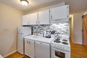 A compact kitchen with white cabinets, a dishwasher, a stove, and a refrigerator.