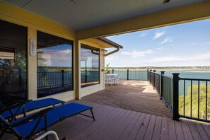 Um deck coberto com vista para a água, uma mesa com cadeiras e uma poltrona azul.