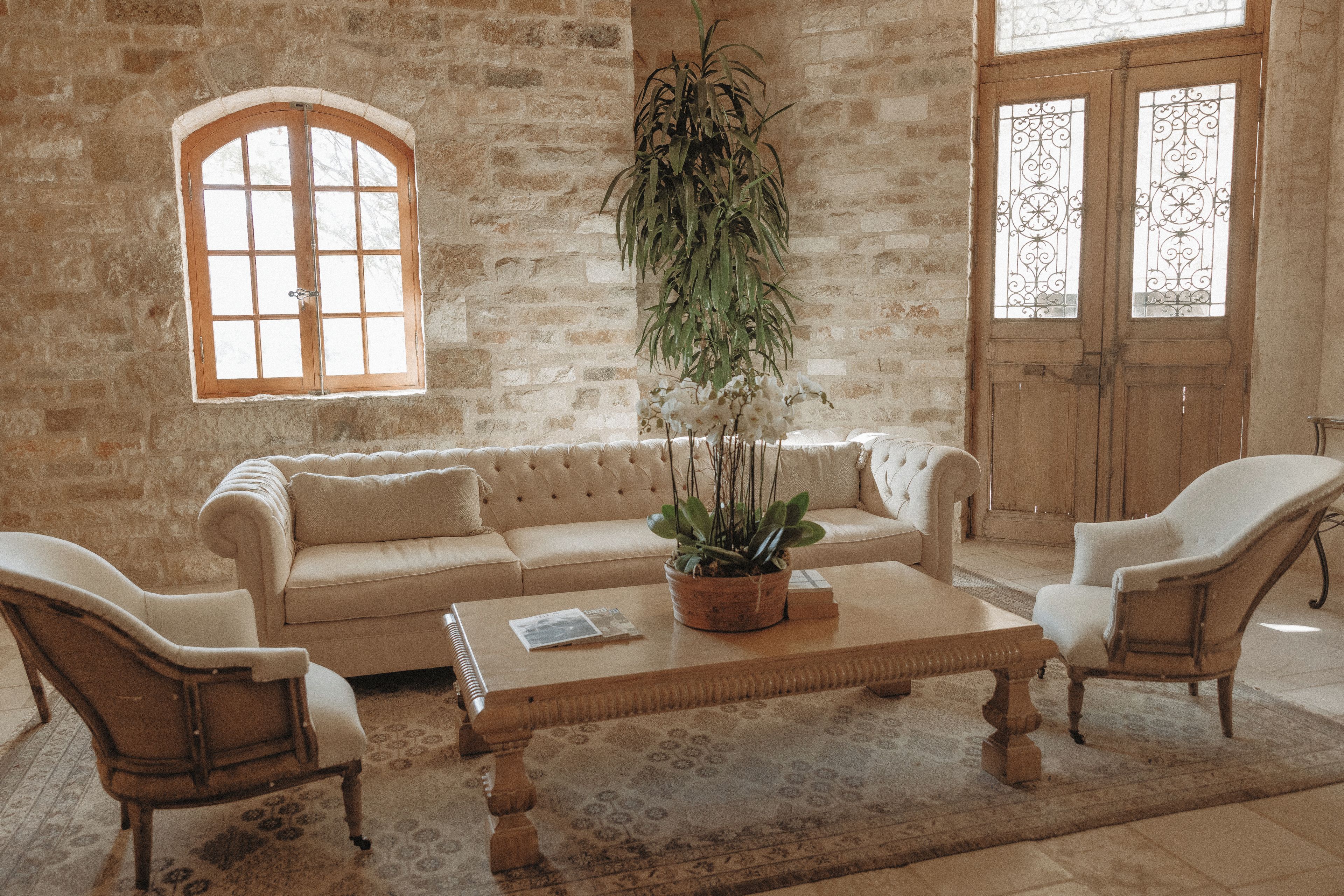 A room with a stone wall, a wooden sofa, two armchairs, a coffee table with a plant, and a window with a view.