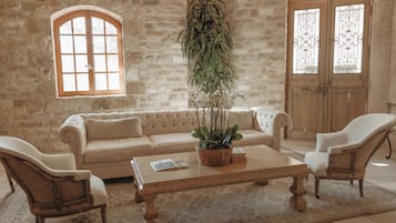 A room with a stone wall, a wooden sofa, two armchairs, a coffee table with a plant, and a window with a view.