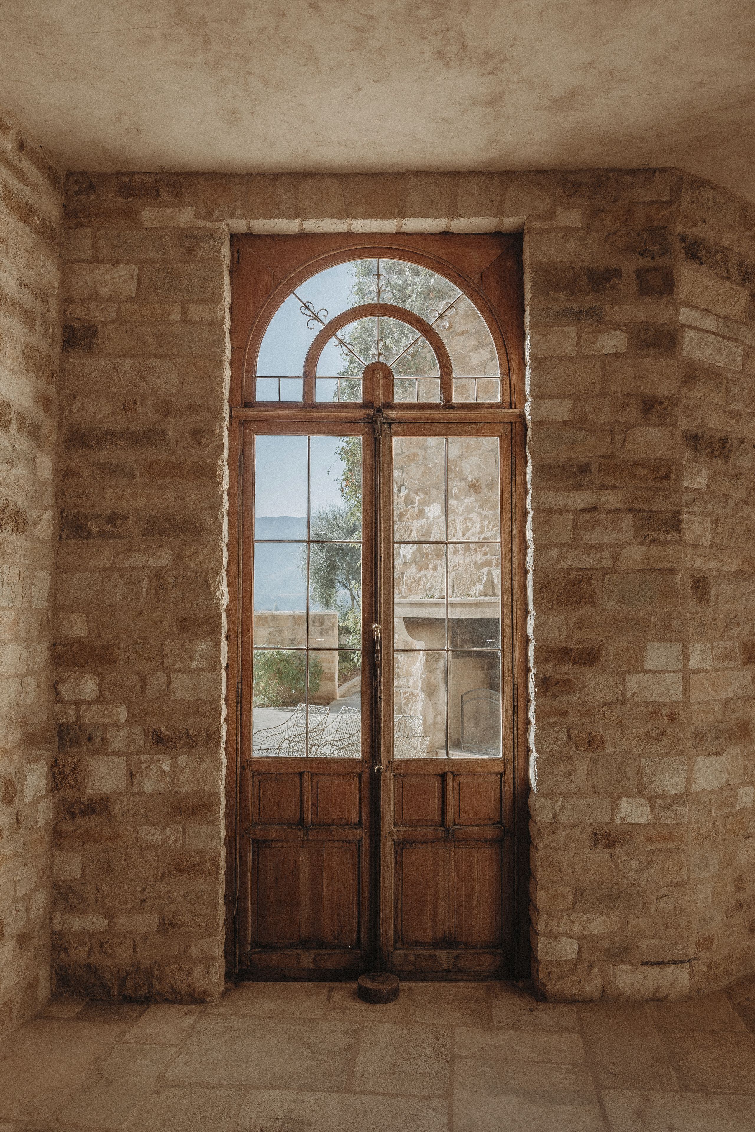 A wooden door with a glass panel, set in a room with stone walls and a tiled floor.