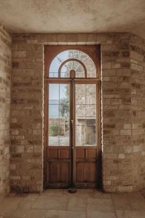 Una puerta de madera con un panel de vidrio, en un espacio con paredes de piedra y suelo de baldosas.