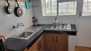 Una cocina con un lavamanos, estufa y ollas colgando.