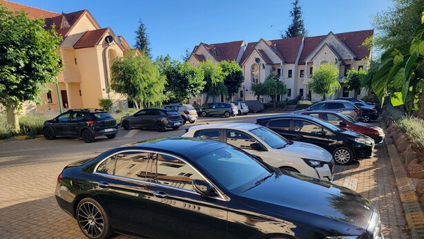 Un estacionamiento con varios coches, un edificio de techo rojo y árboles.