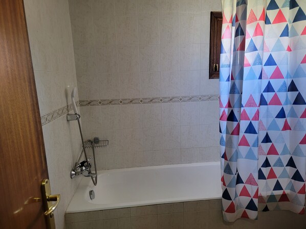 Un baño con bañera, ducha y puerta con pomo de latón.