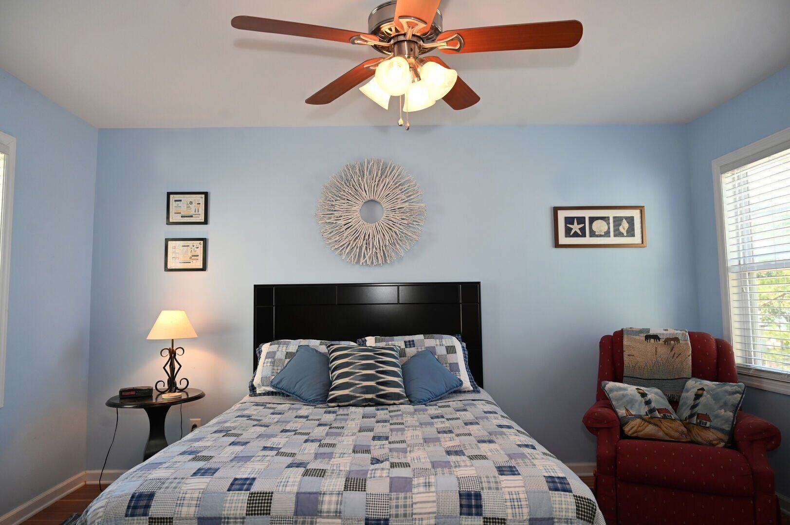 A bedroom with a bed, a ceiling fan, a lamp, a chair, and wall decorations.