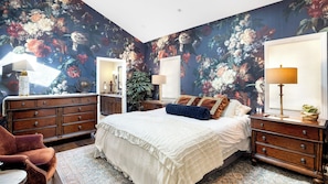 A bedroom with a large bed, two nightstands, a dresser, a chair, and a large mirror.