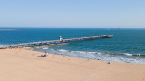 A beach with a pier extending into the ocean, sandy beach, and clear blue water.