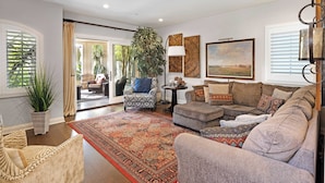 A spacious living room with a large sofa, a patterned rug, and a potted plant.