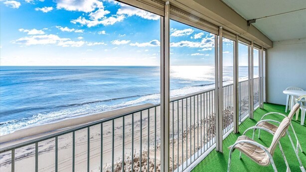 A balcony with a view of the ocean, a table, and two chairs.