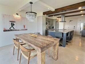 A modern kitchen with a wooden dining table, chairs, and a chandelier. - Elegant 2-Bedroom Beachfront Condo in Sandy Cove (Sarasota)