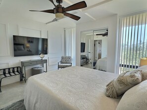 A bedroom with a bed, a desk, a chair, a television, and a ceiling fan.