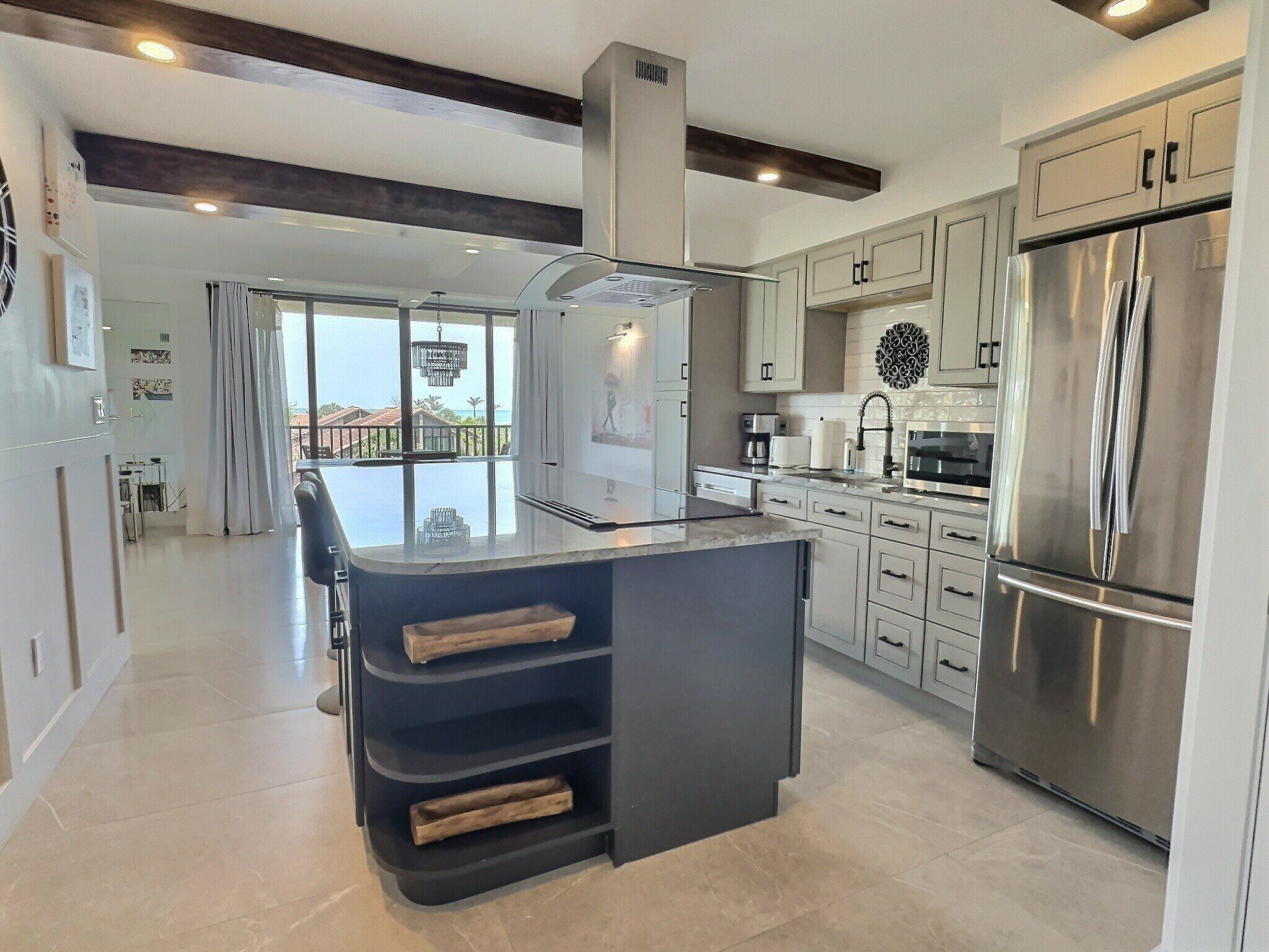 A modern kitchen with a central island, stainless steel appliances, and a view to the outside.