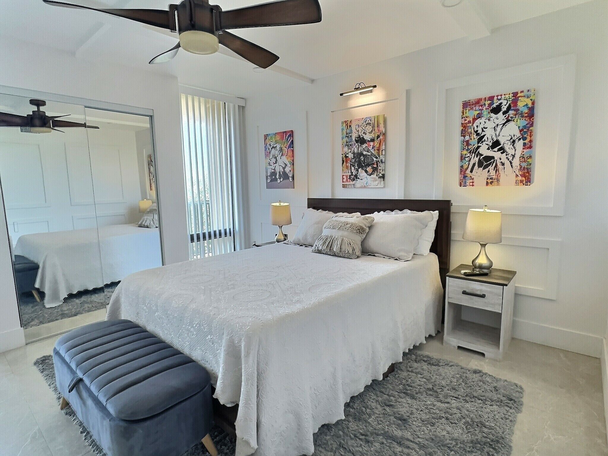 A bedroom with a large bed, two bedside tables with lamps, a ceiling fan, and artwork on the walls.