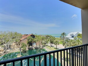 A view from a balcony overlooking a pool, palm trees, and a beach with a clear sky.
