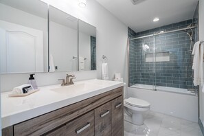 Un baño moderno con tocador blanco, un espejo grande, una ducha con azulejos azules y un inodoro.