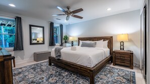 A bedroom with a large bed, a ceiling fan, a nightstand with a lamp, a bedside table, and a window with curtains. - Upscale 2BR Apartment Near Emory Hospital and CDC (Atlanta)