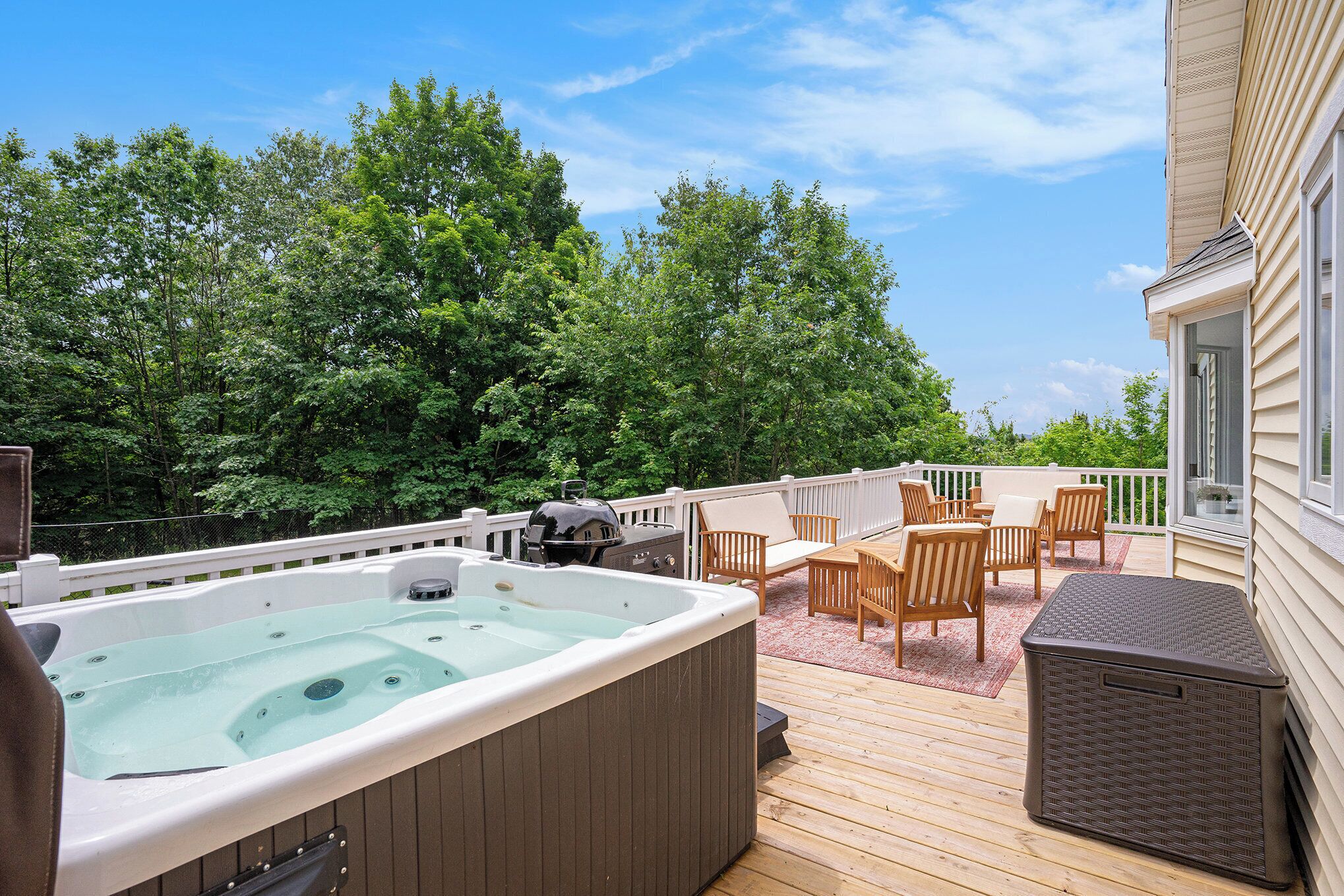 A deck with a hot tub, outdoor furniture, and a view of a forest.
