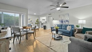 A modern living room with a blue sofa, grey armchairs, a coffee table, and a dining area with a wooden table and chairs.
