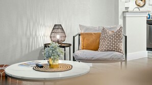 Un salón moderno con una mesa redonda, un sofá con cojines estampados, una lámpara decorativa y una planta pequeña.