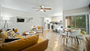 Una sala de estar moderna con un sofá, una mesa de centro y un comedor. Se ve una cocina al fondo con una mesa y sillas.
